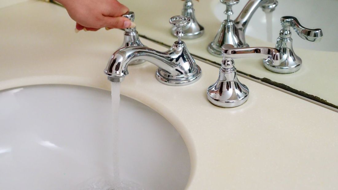 Hand turning on a chrome bathroom faucet