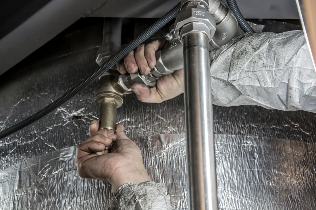 Plumber's hands tightening pipe fittings under a floor